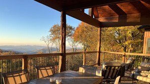 A wooden deck with a table and chairs, overlooking a mountainous landscape. - Buckhorn Lodge - Spacious Luxury Home Near Sugar Mountain Resort, Pool Table, Hot Tub, Views (Sugar Mountain)