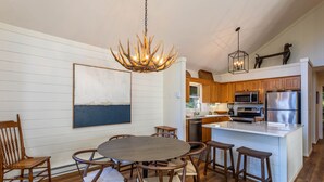 Una cocina moderna con armarios de madera, una isla central con taburetes, una lámpara de araña y un cuadro grande en la pared.