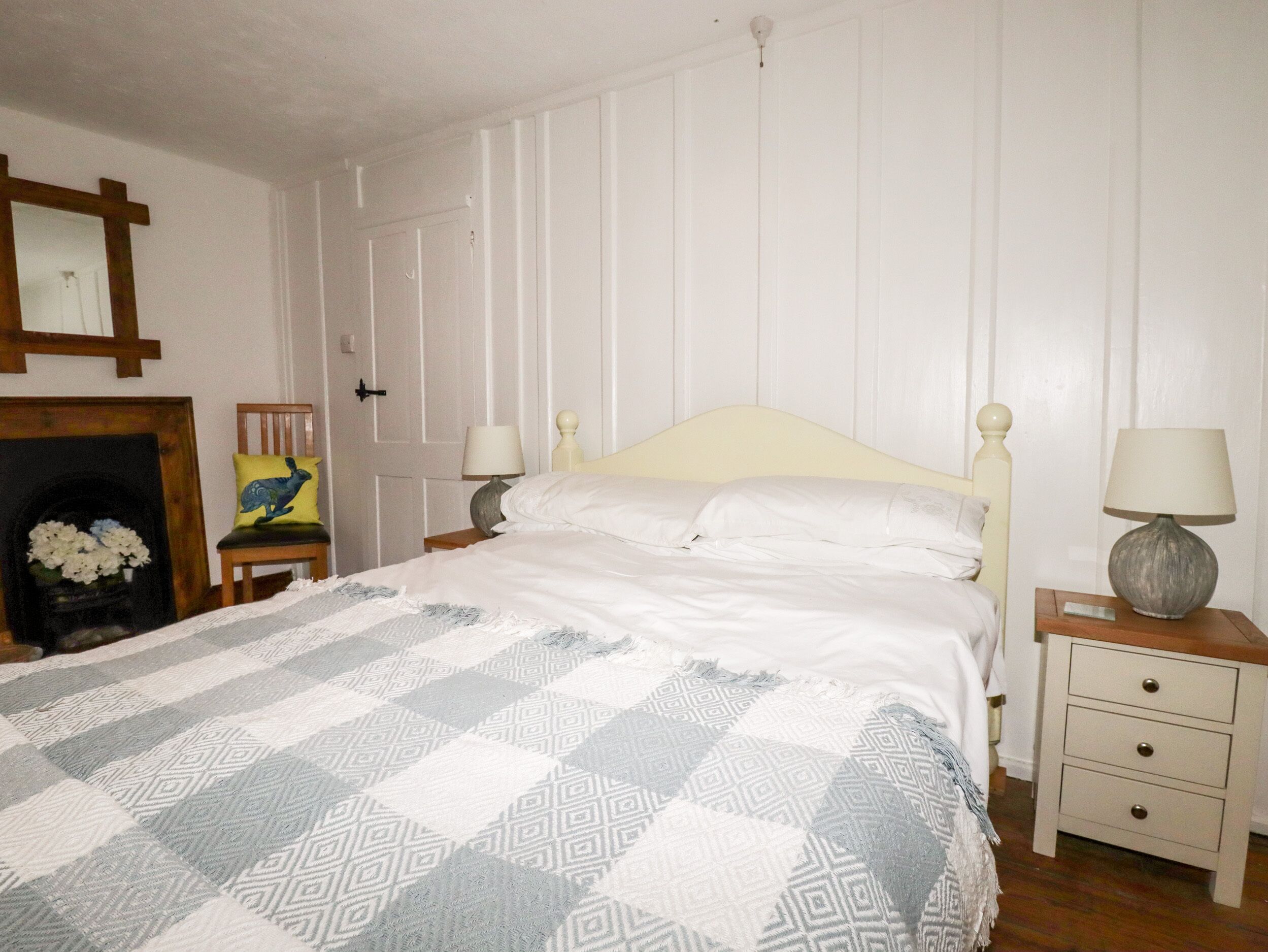 Una cama bien hecha con un edredón estampado, una mesita de noche con una lámpara, y una silla con cojín.