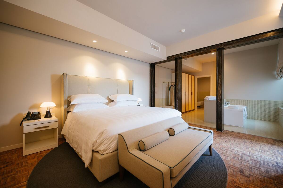 Habitación de hotel moderna con una cama grande, mesitas de noche, un espejo y vista al baño.