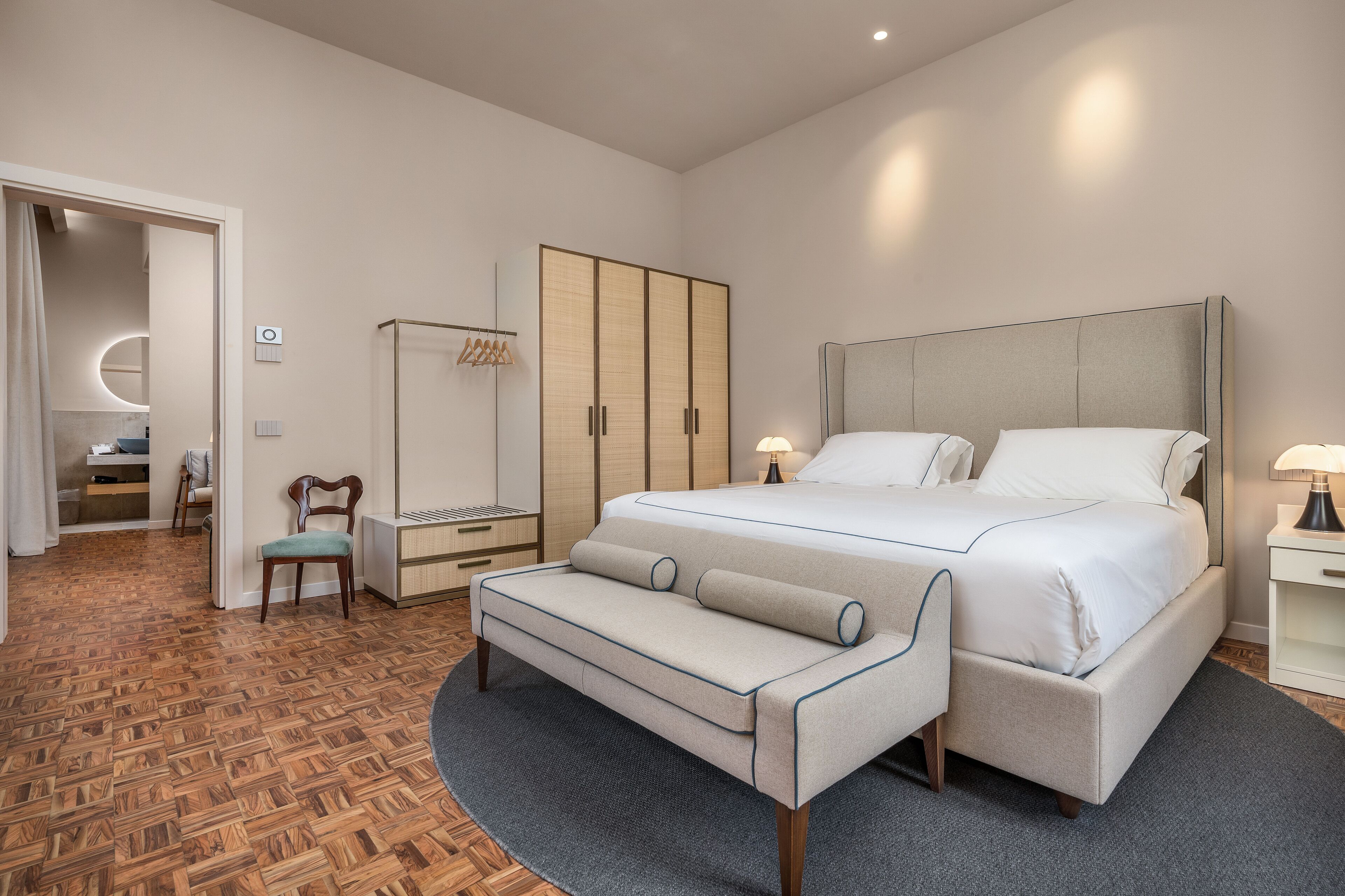 A modern bedroom with a large bed, bedside tables, a wardrobe, and a seating area.