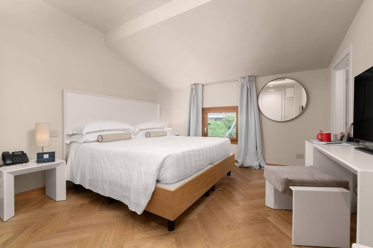 Un dormitorio moderno con cama, mesita de noche, escritorio y un espejo redondo.
