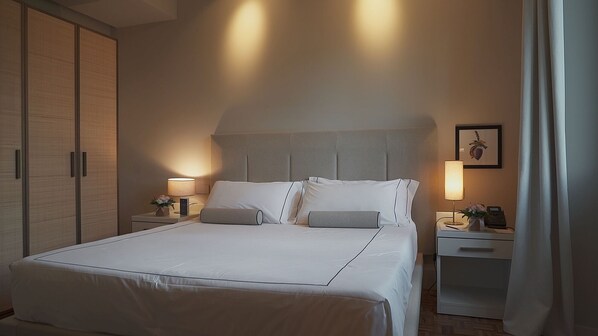A hotel room with a large bed, two bedside tables, a nightstand, a wardrobe, and a framed picture on the wall.
