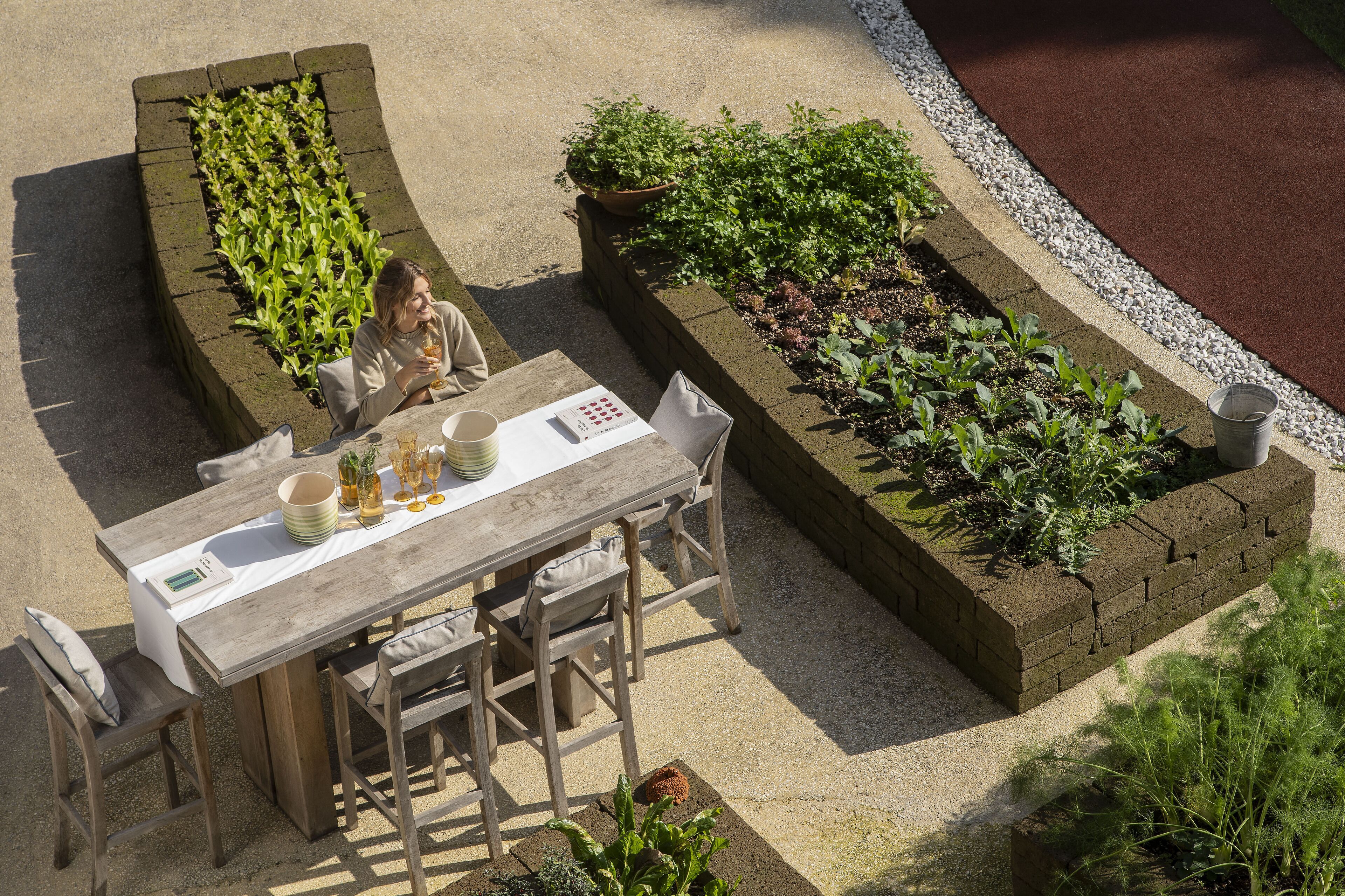 Ein Essbereich im Freien mit Tisch und Stühlen, umgeben von erhöhten Blumenbeeten mit verschiedenen Pflanzen.
