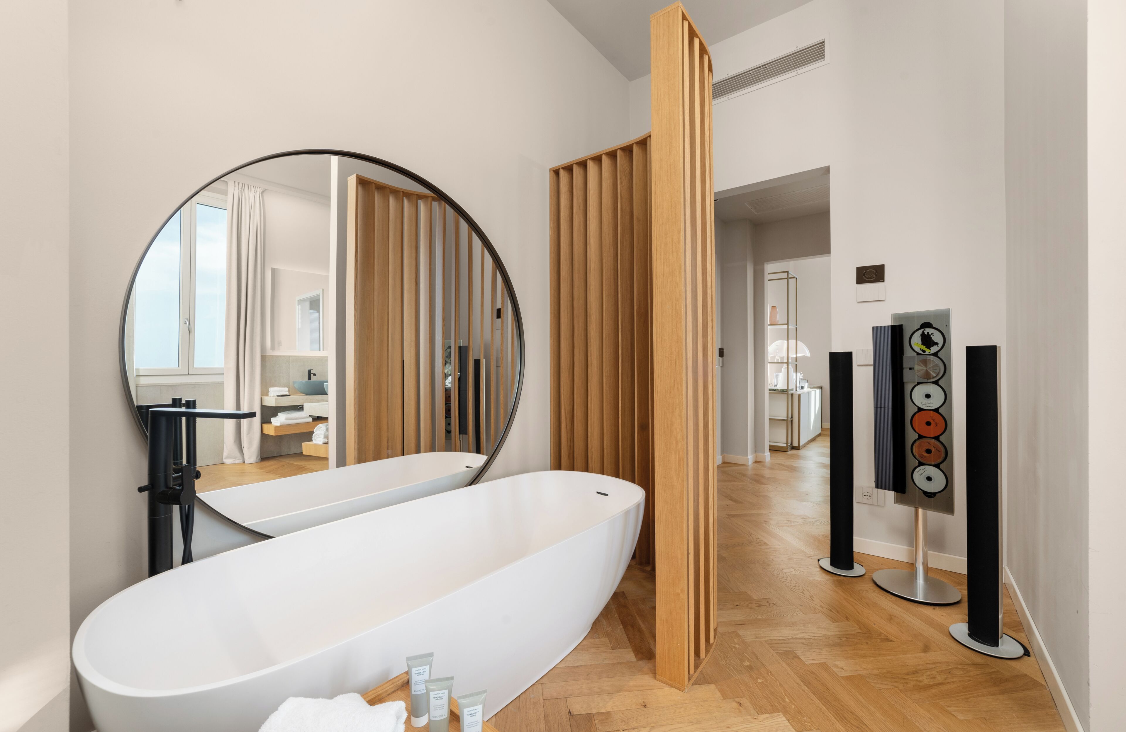 Un baño moderno con una bañera independiente, un espejo grande, paneles de madera y un sistema de sonido.