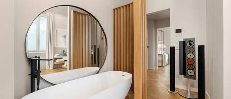 Un baño moderno con una bañera independiente, un espejo grande, paneles de madera y un sistema de sonido.