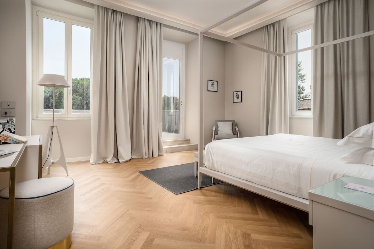 Una habitación de hotel moderna con cama, escritorio, silla y ventanas grandes con cortinas.