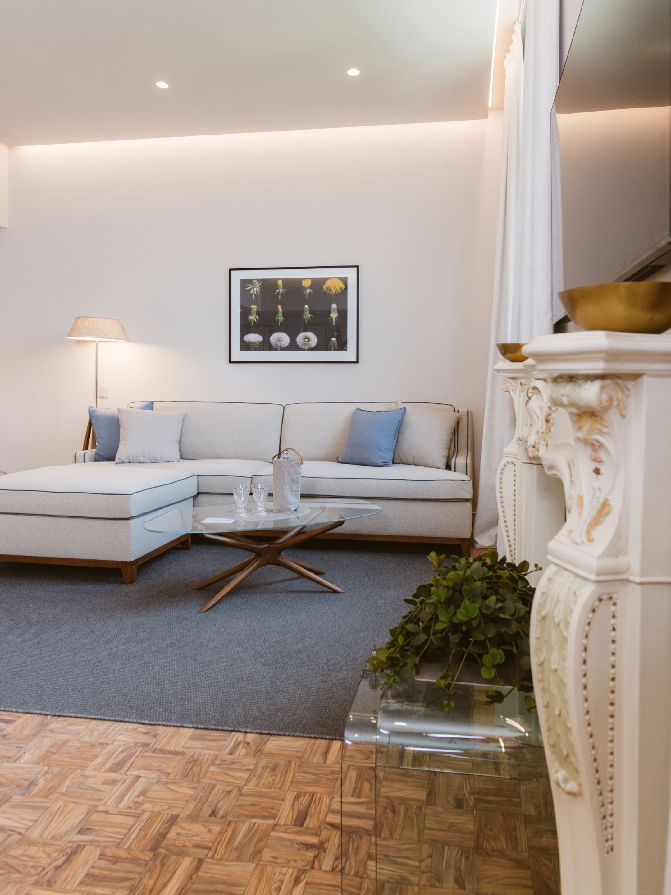 A modern living room with a sectional sofa, a glass coffee table, a floor lamp, and a framed floral artwork on the wall.