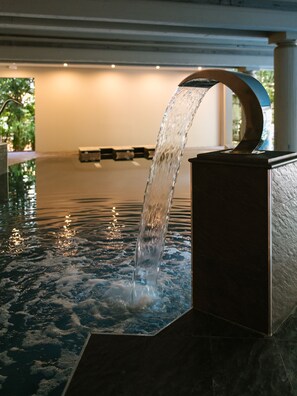 Ein Wasserspiel mit gebogener Tülle, rechteckigem Becken und einem spiegelnden Teich.