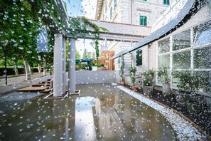 Un espacio al aire libre cubierto con suelo de hormigón, plantas en macetas y una pérgola de madera.
