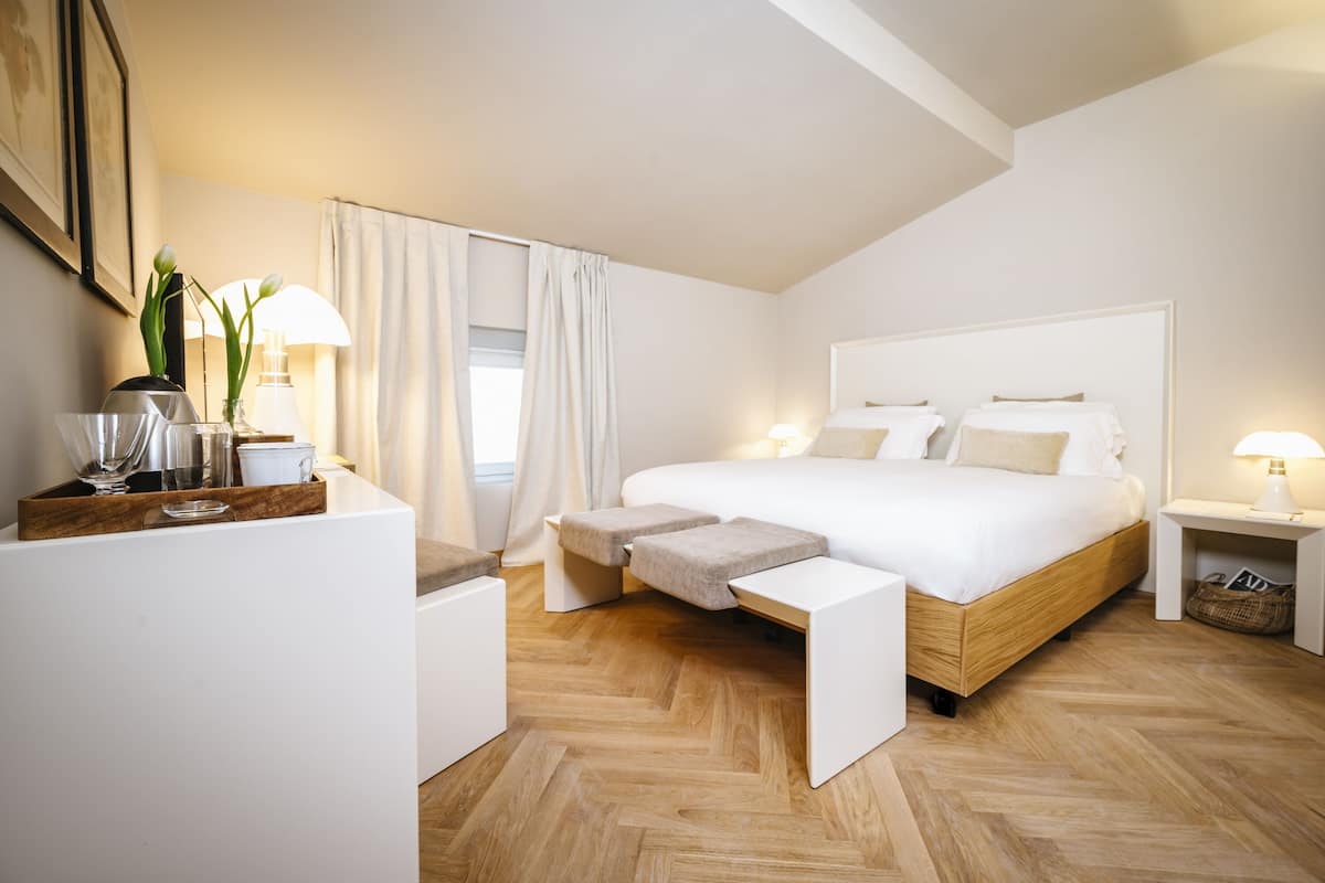 Un dormitorio moderno con una cama grande, mesitas de noche, un escritorio con lámpara y una ventana con cortinas.