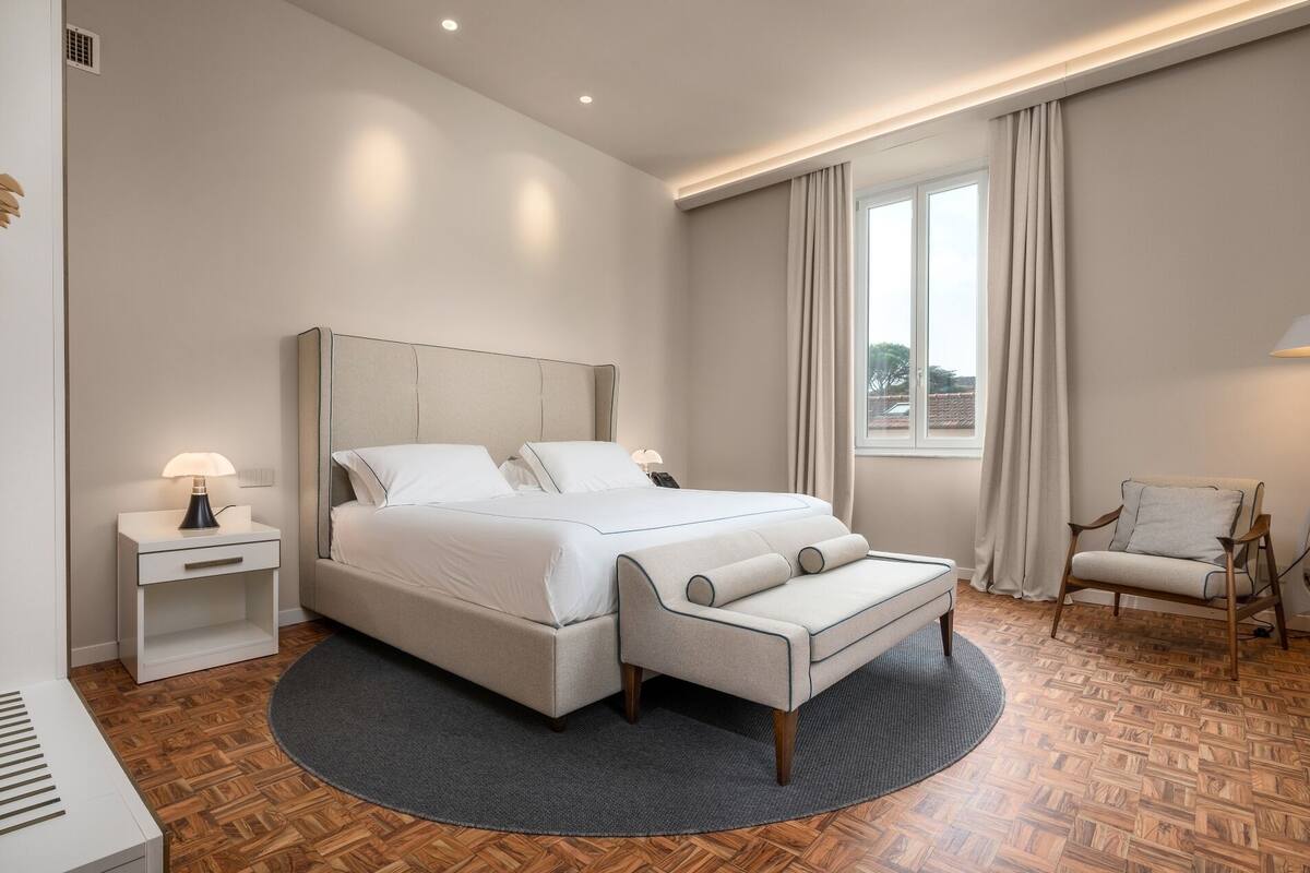 Un dormitorio moderno con una cama grande, mesitas de noche, una silla y vistas al exterior.