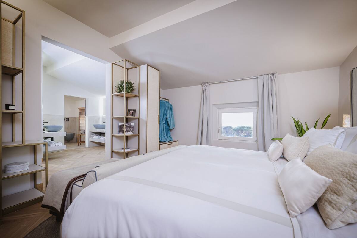 Un dormitorio moderno con una cama grande, estanterías empotradas, un ventanal con cortinas y vistas al baño.