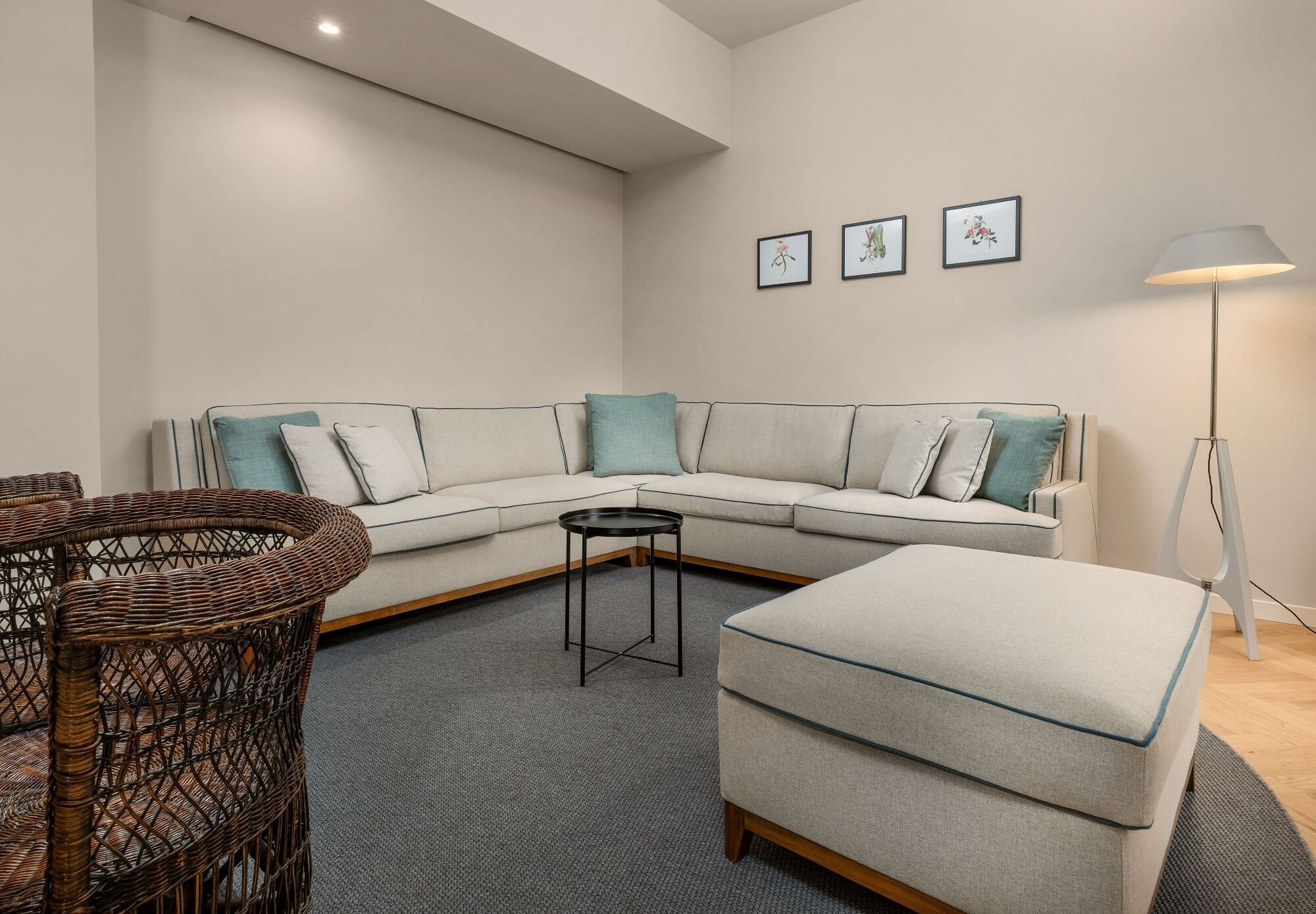 A modern living room with a sectional sofa, a round wicker chair, a small side table, and a floor lamp.