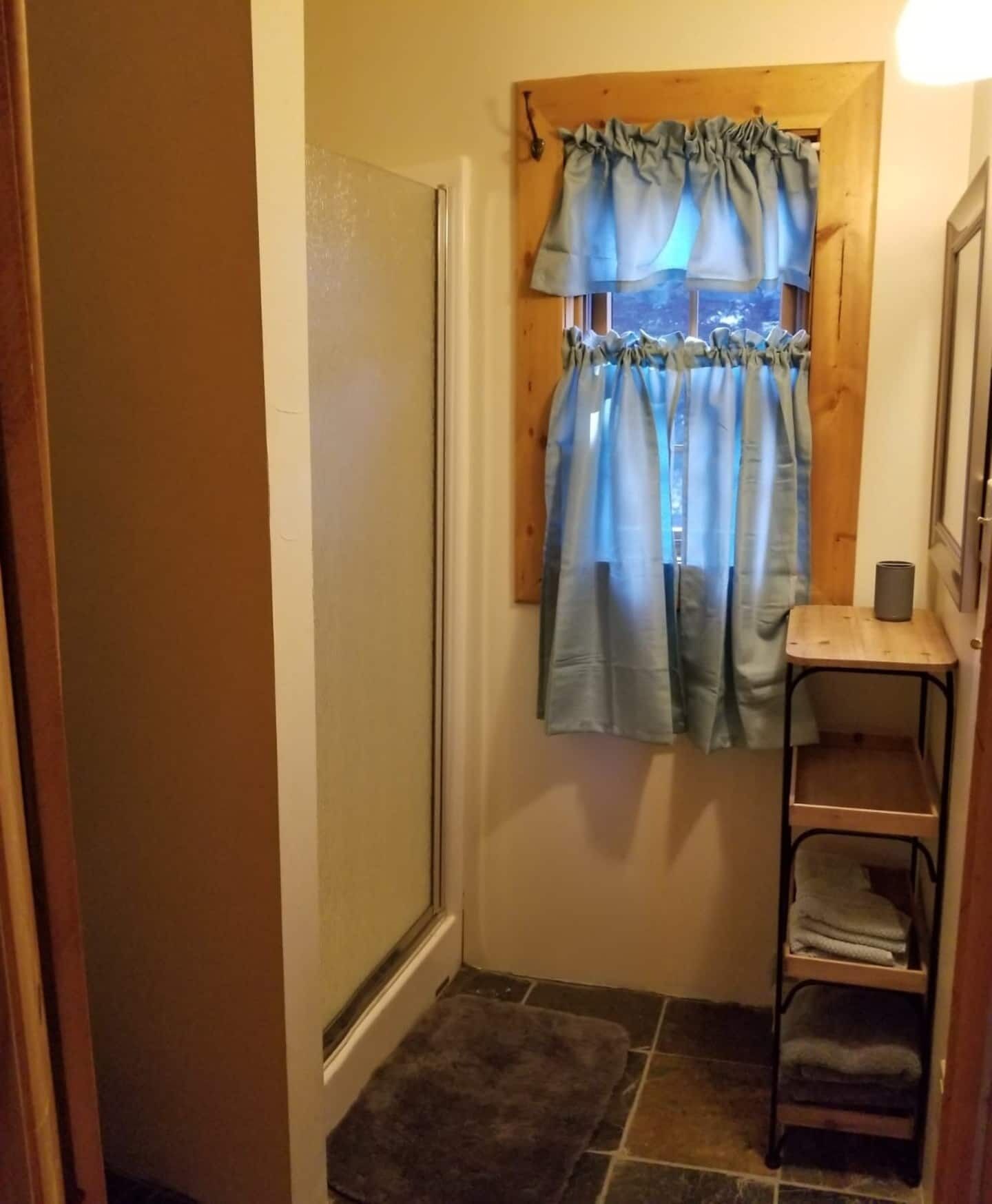 A bathroom with a shower, a towel rack, a mirror, and a small shelf with towels.