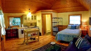 Un accogliente chalet dall'interno in legno, con angolo cottura, zona pranzo e camera da letto con un letto e un divano.