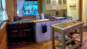 Una cucina accogliente con pavimento in legno, un'isola centrale, sgabelli da bar, una macchina da caffè e un lampadario.