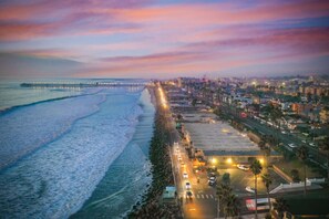Paisagem costeira com praia, um cais e um estacionamento cheio de carros.