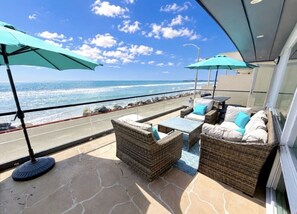 A balcony with wicker furniture, two umbrellas, and a view of the ocean.