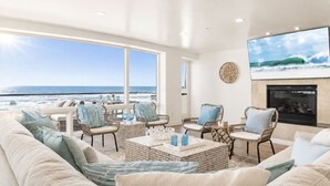 A spacious living room with a large window overlooking the ocean, furnished with a sofa, chairs, and a coffee table.