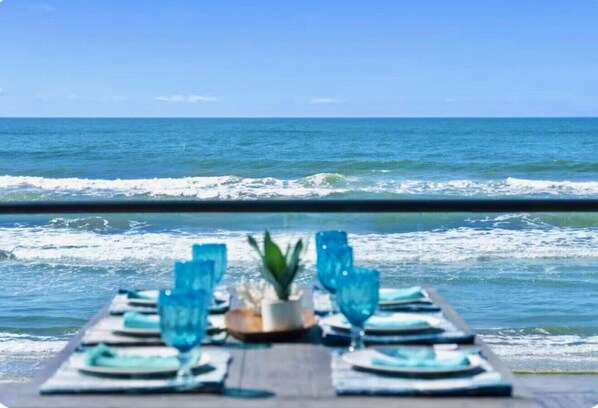 Mesa posta com copos e pratos azuis, com vista para o oceano.