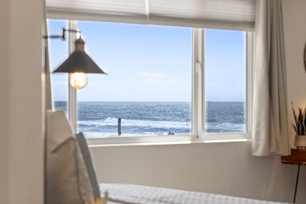Habitación con un amplio ventanal con vistas al mar, una cama, una lámpara y una pequeña mesa con una planta.