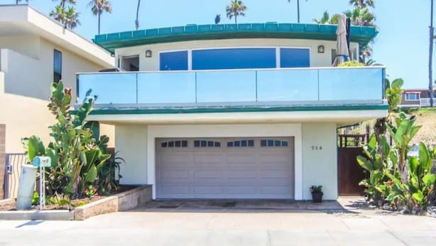 A two-story house with a garage, surrounded by palm trees and a clear sky.