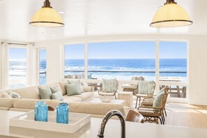 Uma sala de estar ampla com uma grande janela com vista para o oceano, mobiliada com um sofá, cadeiras e uma mesa de centro.