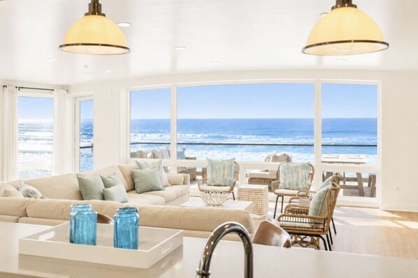 A spacious living area with a large window overlooking the ocean, furnished with a sofa, chairs, and a coffee table.