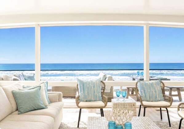 A room with a view of the ocean, featuring a sofa, chairs, and a table with decorative items.