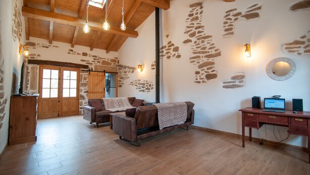 A rustic interior with a wooden ceiling, stone wall accents, a sofa, a desk with a laptop, and a wooden cabinet. - Vintage Cottage With Large Yard (Cerezal de Peñahorcada)