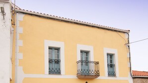 A two-story building with a yellow facade, a blue door, and a balcony with black railings. - Vintage Cottage With Large Yard (Cerezal de Peñahorcada)