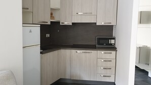 A compact kitchen with light wood cabinets, a black countertop, and a built-in microwave. - Lupetta apartment (Milan)