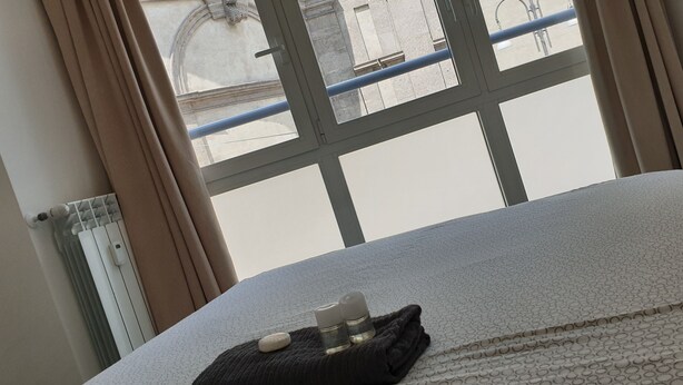 A hotel room with a bed, a window with curtains, and a radiator. - Lupetta apartment (Milan)