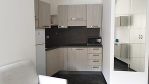 A compact kitchen with light wood cabinets, a black countertop, and a built-in microwave. - Lupetta apartment (Milan)
