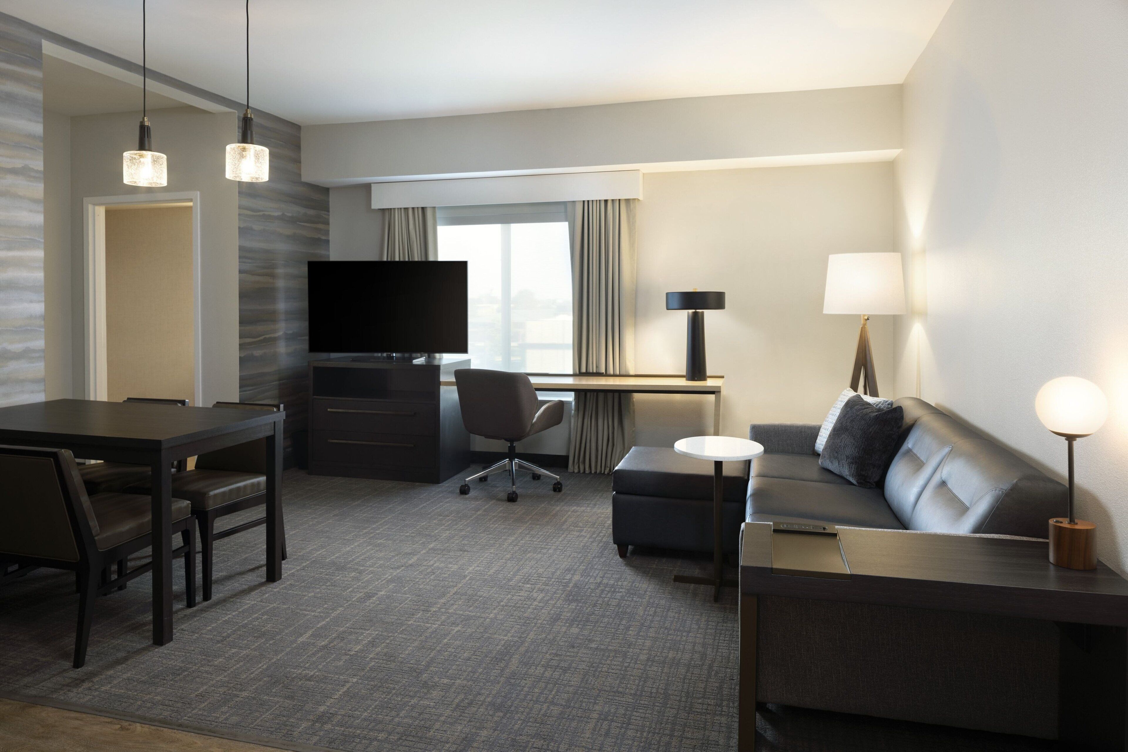 Een hotelkamer met een eettafel, een bank, een bureau met een computer, een televisie en een lamp.