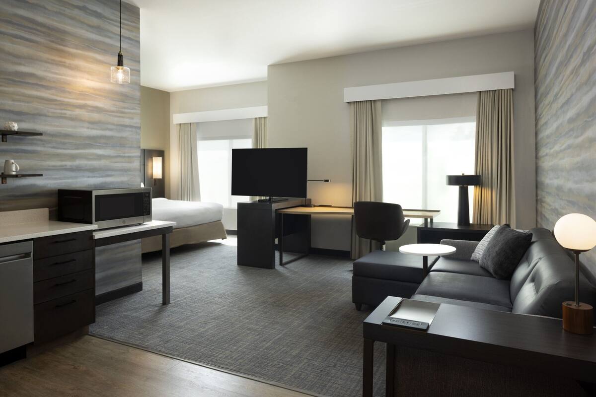 A modern hotel room with a flat-screen TV, a desk, a sofa, and a dining area.