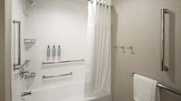 A modern bathroom with a bathtub, shower, and toilet. It includes a towel rack, handrails, and a shower curtain.