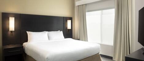 Une chambre d’hôtel avec un grand lit, deux tables de chevet avec des lampes, un téléviseur à écran plat et une grande fenêtre avec des rideaux.