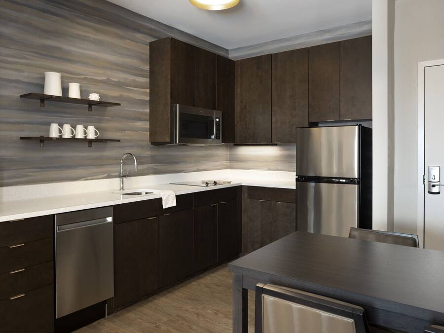 A modern kitchen with dark cabinetry, stainless steel appliances, and a marble backsplash.