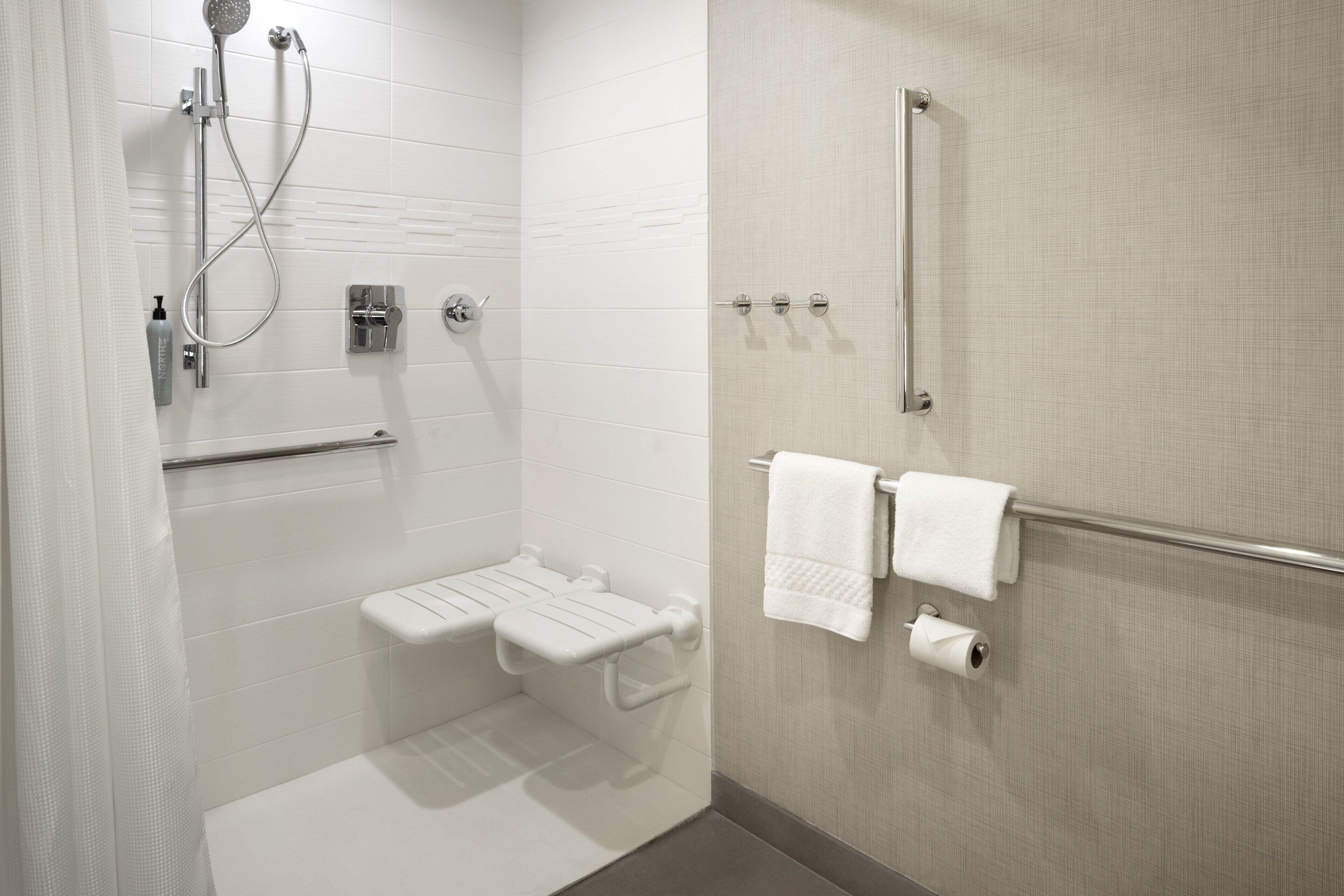 A modern bathroom with a shower, toilet, and grab bars.