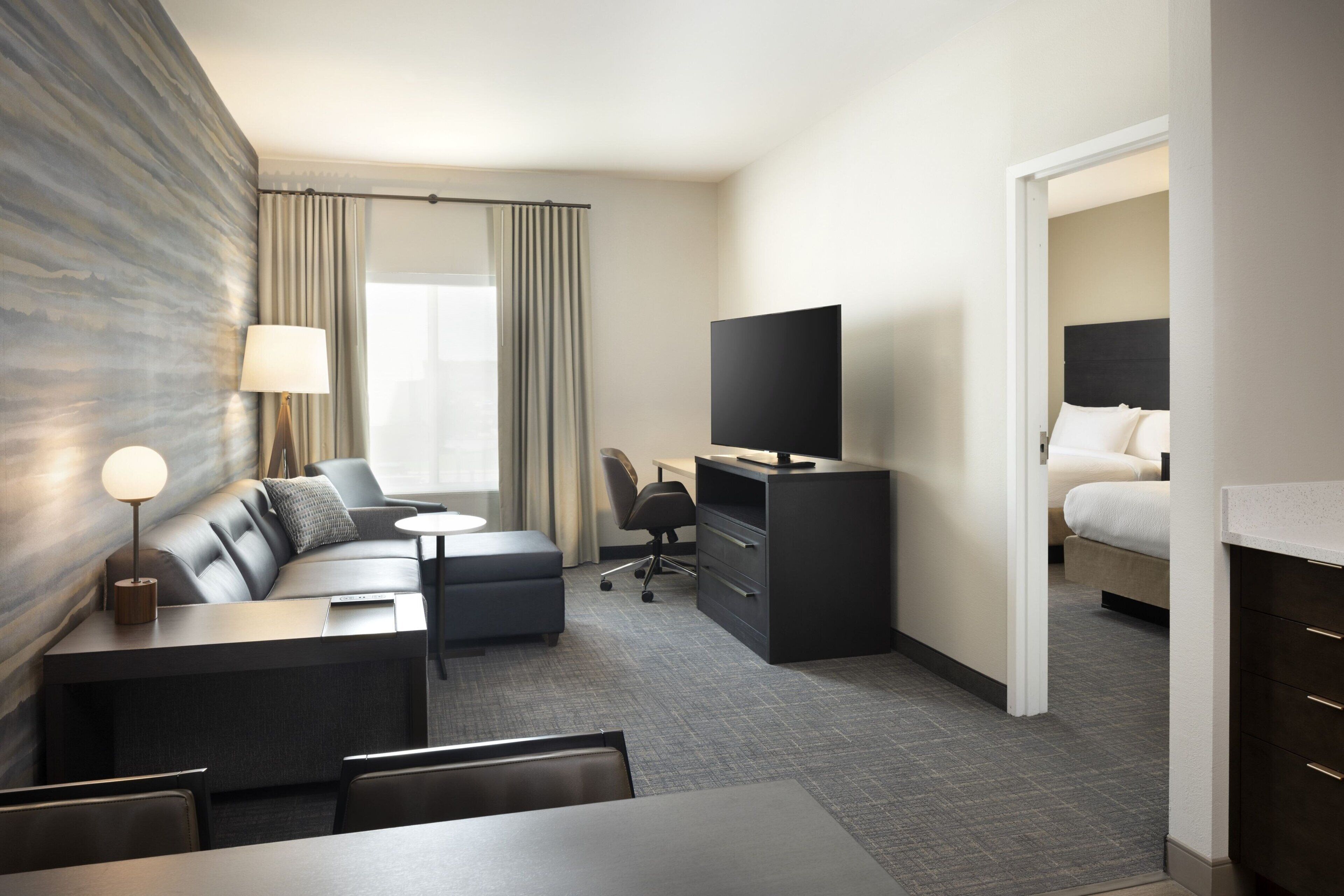 A hotel room with a sofa, a desk, a television, a bed, and a desk lamp.