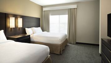 Een hotelkamer met twee bedden, een nachtkastje, een televisie en een groot raam met gordijnen.