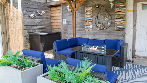 Un espace extérieur aménagé avec des canapés bleus dotés de coussins moelleux, une table en verre avec un foyer intégré et des éléments décoratifs muraux.
