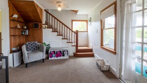 Un vaste espace de vie agrémenté d’un escalier en bois, d’un canapé gris et d’un meuble de rangement intégré où sont pliées des couvertures.