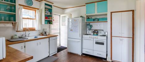 Una cocina compacta con armarios blancos, un refrigerador, una estufa y un lavaplatos.