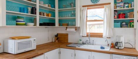 A compact kitchen with white cabinets, a microwave, a sink, and a coffee maker. Shelves above the sink hold various kitchen items.