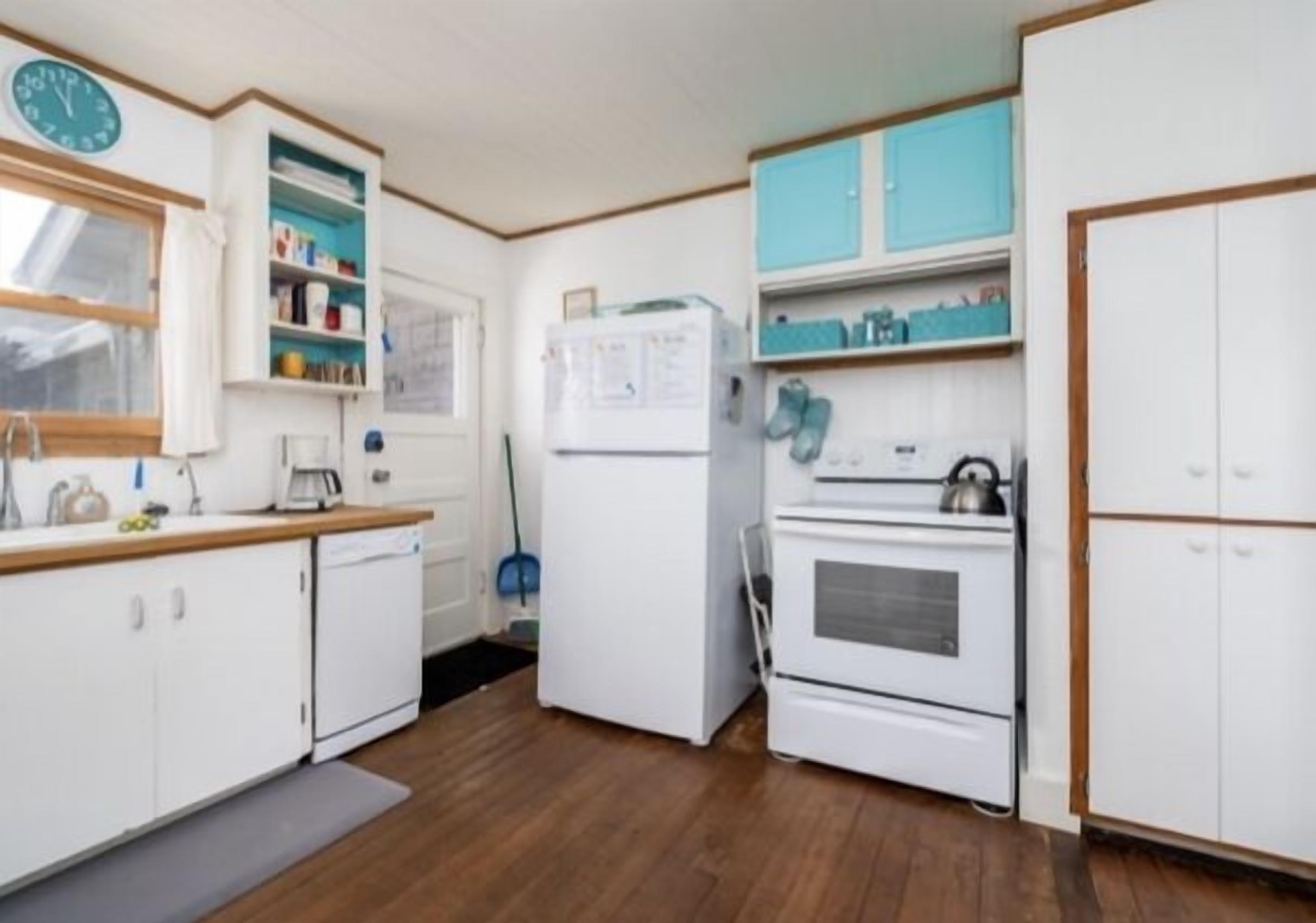 Una cocina compacta con armarios blancos, un refrigerador, un horno y un reloj en la pared.
