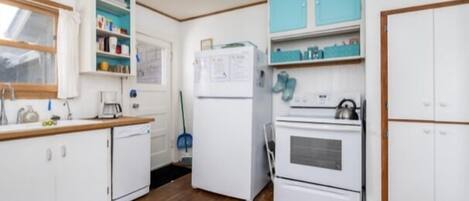 Una cocina compacta con armarios blancos, un refrigerador, un horno y un reloj en la pared.