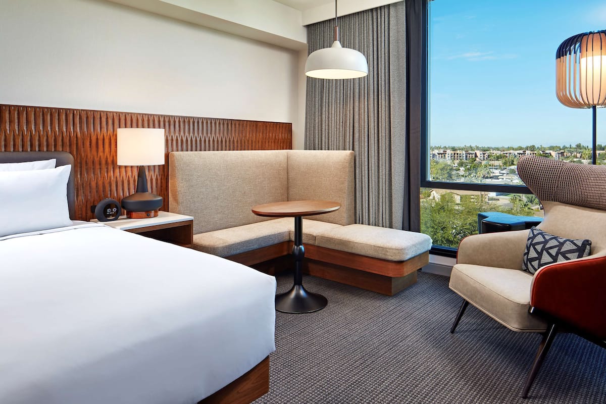 Ein Hotelzimmer mit Bett, Sofa, einem kleinen runden Tisch, einer Lampe und Blick auf die Stadt.